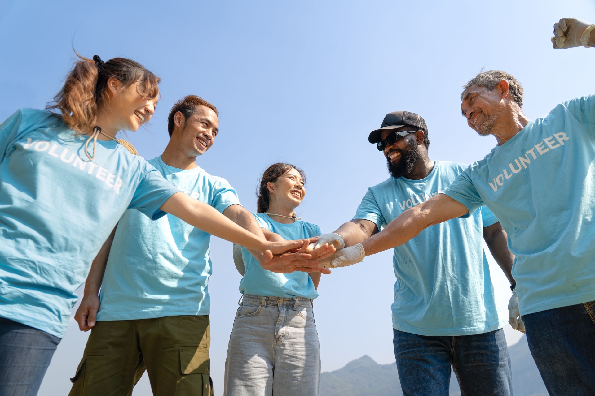 Group of happy diverse volunteers joining hands stack together and raising hands with smile